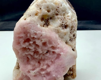 May include: A natural stone with a rough, textured surface. The stone features a prominent section of light pink color, contrasting with the beige and brown areas. The overall shape is irregular, showcasing the raw, unpolished nature of the mineral.