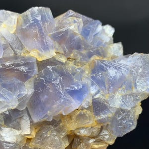 May include: Close-up of a cluster of blue and yellow fluorite crystals. The crystals have a cubic structure and a translucent appearance, with variations in color and texture. The overall composition is a natural mineral formation.