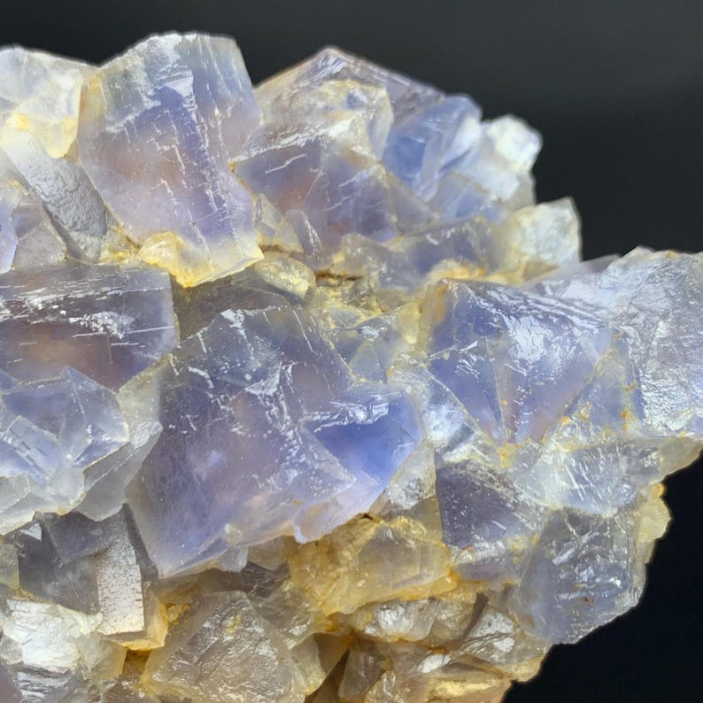 May include: Close-up of a cluster of blue and yellow fluorite crystals. The crystals have a cubic structure and a translucent appearance, with variations in color and texture. The overall composition is a natural mineral formation.