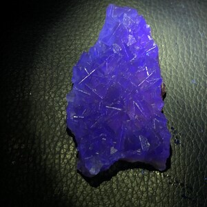 K&ouml;nnte beinhalten: Ein lebendiger, unregelm&auml;&szlig;ig geformter, tiefblauer Kristallcluster. Der Kristall hat eine raue, strukturierte Oberfl&auml;che mit sichtbaren Kristallstrukturen und einem dunklen Hintergrund.