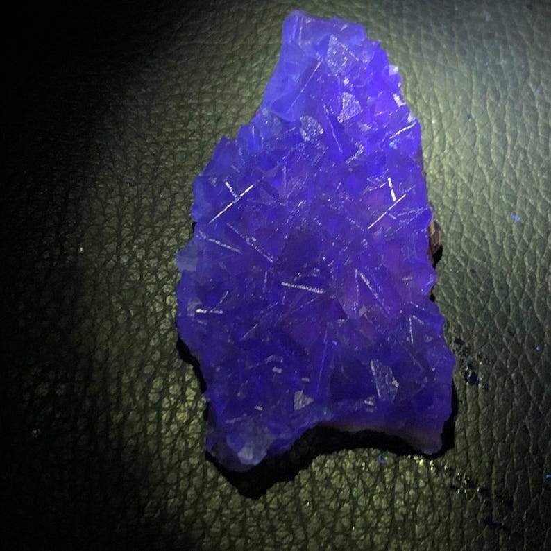 K&ouml;nnte beinhalten: Ein lebendiger, unregelm&auml;&szlig;ig geformter, tiefblauer Kristallcluster. Der Kristall hat eine raue, strukturierte Oberfl&auml;che mit sichtbaren Kristallstrukturen und einem dunklen Hintergrund.