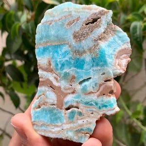 May include: A raw, flat slab of blue hemimorphite mineral featuring horizontal bands of vibrant turquoise and light blue crystalline structures interspersed with earthy brown, tan, and beige mineral deposits across its textured surface.