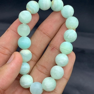 May include: A bracelet of pale green, spherical beads. The beads are a soft, pastel green hue and appear to be made of natural stone. The bracelet is strung together to form a complete circle, and is a light green colour.