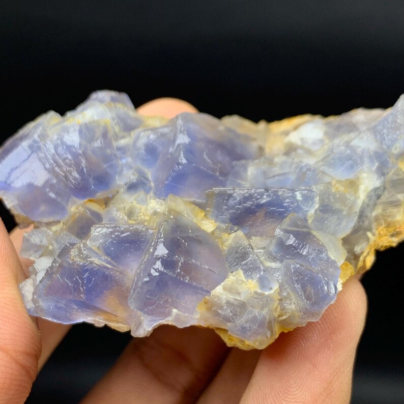 May include: A close-up of a blue and white fluorite mineral specimen. The fluorite crystals have a translucent quality, with a mix of light and dark blue hues. The mineral sits on a light brown matrix, with a dark background.
