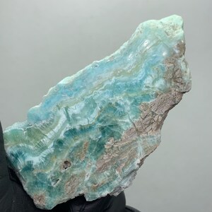 May include: A raw, natural mineral specimen with a layered appearance. The stone features shades of blue, green, and brown, with a textured surface. The mineral's colors and patterns create a unique, organic aesthetic, suitable for collectors or decorative purposes.