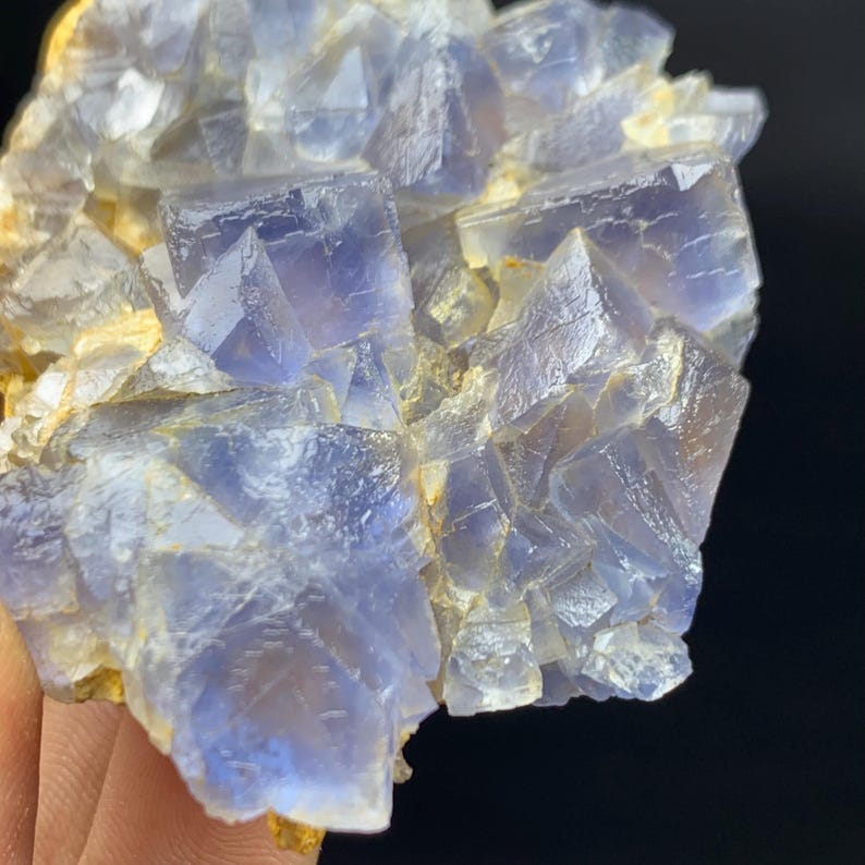 May include: Close-up of a natural fluorite crystal cluster. The crystal features a mix of translucent blue and clear cubic formations, with a pale yellow matrix. The facets of the crystals reflect light, creating a sparkling effect.
