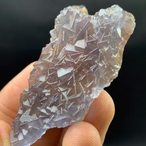 K&ouml;nnte beinhalten: Nahaufnahme eines Fluorit-Kristallclusters. Der Kristall hat eine komplexe, geometrische Struktur mit einer Mischung aus lila und klaren Farbt&ouml;nen. Die Kanten des Kristalls sind rau und uneben, mit einer nat&uuml;rlichen, organischen Form. Der Hintergrund ist dunkel.