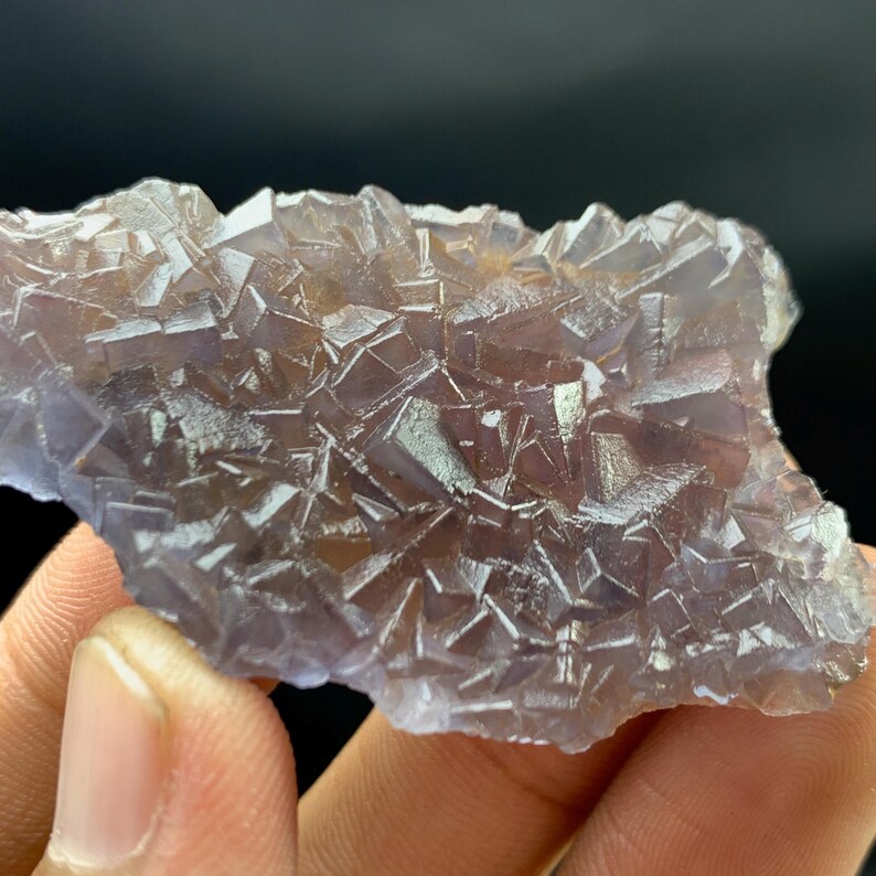K&ouml;nnte beinhalten: Nahaufnahme eines Fluorit-Kristallclusters. Der Kristall hat eine komplexe geometrische Struktur mit vielen kleinen, quadratischen Kristallen. Die Farbe ist eine Mischung aus Lila und Braun, mit einer durchscheinenden Qualit&auml;t. Der Hintergrund ist schwarz.