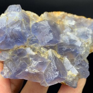 May include: A close-up of a natural fluorite crystal cluster. The crystal features a mix of blue and clear crystalline structures with a rough, textured surface. The mineral specimen has a natural, raw appearance.