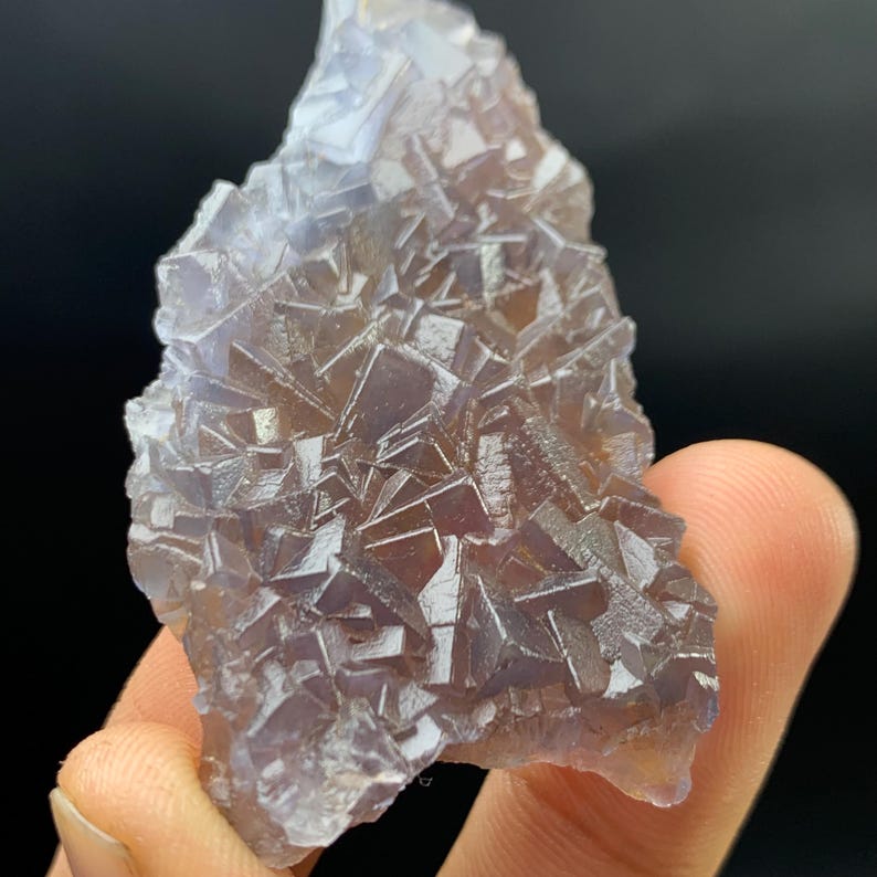 K&ouml;nnte beinhalten: Nahaufnahme eines Fluorit-Kristallclusters. Der Kristall hat eine komplexe, geometrische Struktur mit einer Mischung aus lila und braunen Farbt&ouml;nen. Die Oberfl&auml;che des Kristalls ist rau und strukturiert, mit vielen kleinen, einzelnen Kristallfl&auml;chen sichtbar.