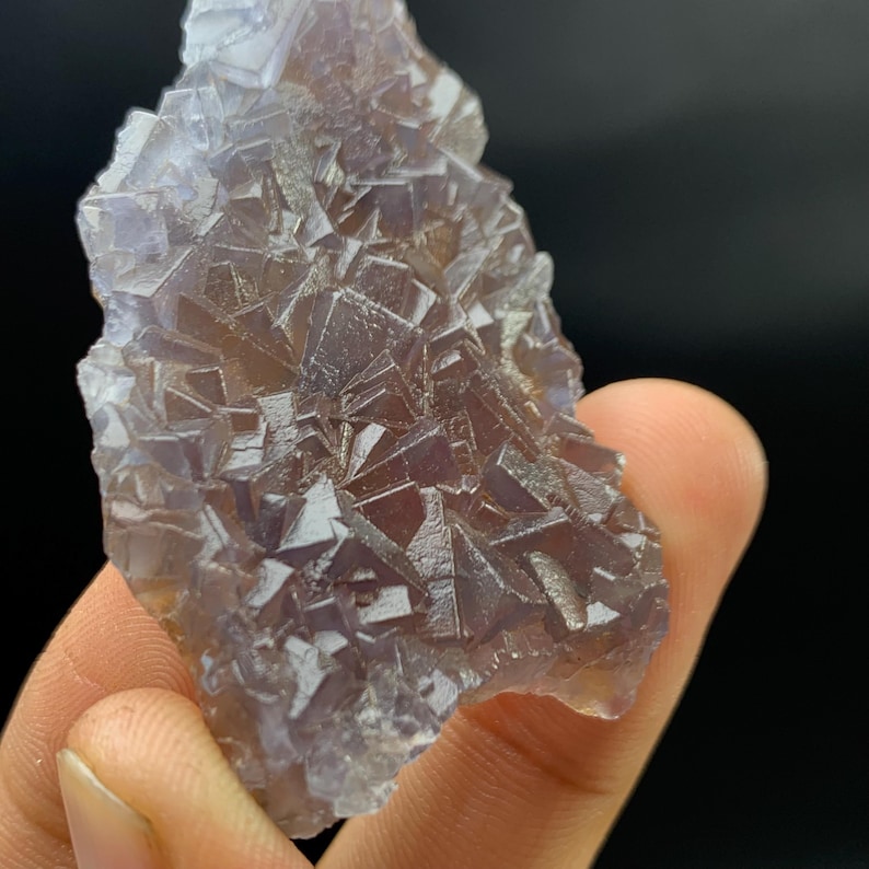K&ouml;nnte beinhalten: Nahaufnahme eines Fluorit-Kristallclusters. Der Kristall hat eine komplexe, geometrische Struktur mit einer Mischung aus lila und klaren Farbt&ouml;nen. Die Oberfl&auml;che des Kristalls ist rau und strukturiert, mit vielen kleinen, einzelnen Kristallfl&auml;chen sichtbar.