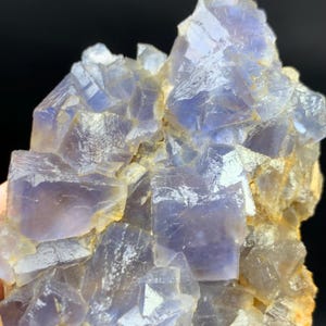 May include: Close-up of a cluster of blue and purple fluorite crystals. The crystals have a cubic structure and are partially translucent, with a light yellow matrix. The mineral formation is set against a dark background.