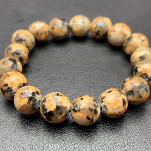 Op de afbeelding: Een armband met ronde, gespikkelde kralen in tinten van bruin, beige en zwart. De gepolijste stenen kralen zijn geregen om een cirkelvorm te vormen. De kralen hebben een diameter van ongeveer 2 cm. Een sieraad.