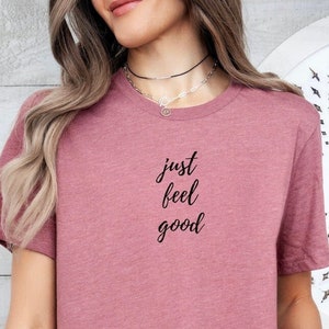 May include: A mauve colored t-shirt with the text "just feel good" printed on the front.
