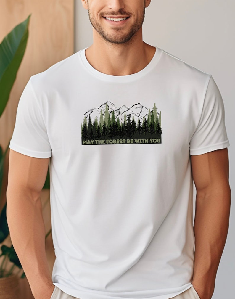 May include: White t-shirt with a green and black mountain and forest graphic. The text "May the forest be with you" is printed below the graphic.