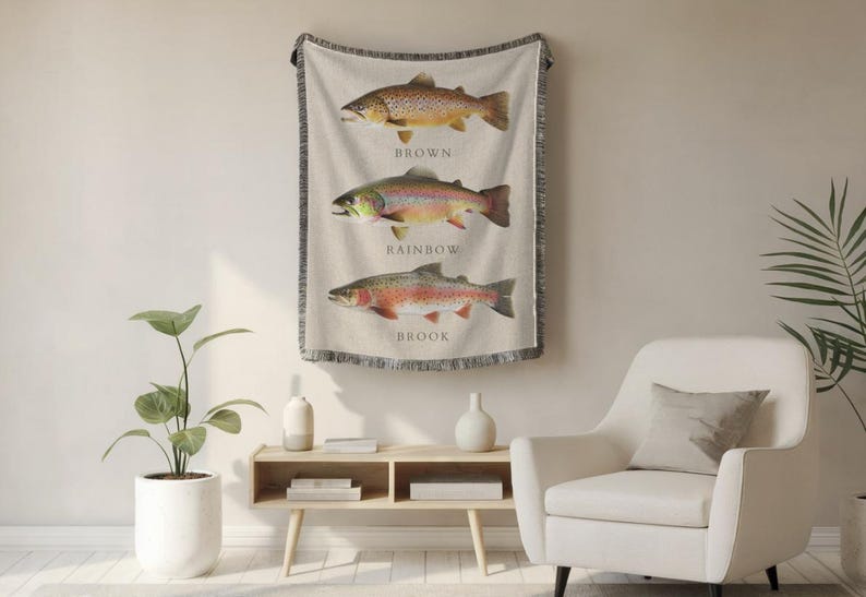 May include: A woven wall tapestry featuring three different types of trout: brown, rainbow, and brook. Each fish is depicted in a realistic style with detailed markings and colours. The tapestry has a fringed border and is hung on a white wall.
