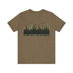 May include: A brown t-shirt with a green and brown mountain and forest graphic. The text "May the forest be with you" is printed below the graphic.