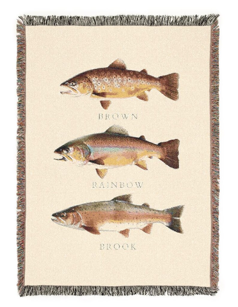 May include: A woven tapestry featuring three different types of trout: a brown trout, a rainbow trout, and a brook trout. Each fish is depicted in detail with realistic colours and markings. The tapestry has a cream-coloured background and a brown fringe border.