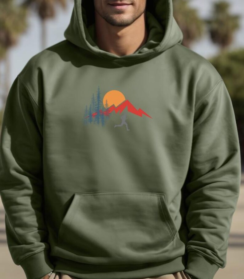 May include: A green hooded sweatshirt with a graphic design of a mountain range, a sun, and trees. The graphic is in shades of red, orange, blue, and white.