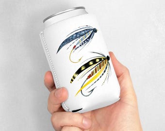 以下が含まれることがあります： 2 つの釣りフライの水彩イラストが描かれた白い缶クーラー。1 つのフライは青と黄色のアクセントがあり、もう 1 つは黒と黄色のアクセントがあります。缶クーラーは手で持たれています。