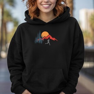 May include: Black hooded sweatshirt with a graphic of a person running in front of a mountain range with a sun and trees.
