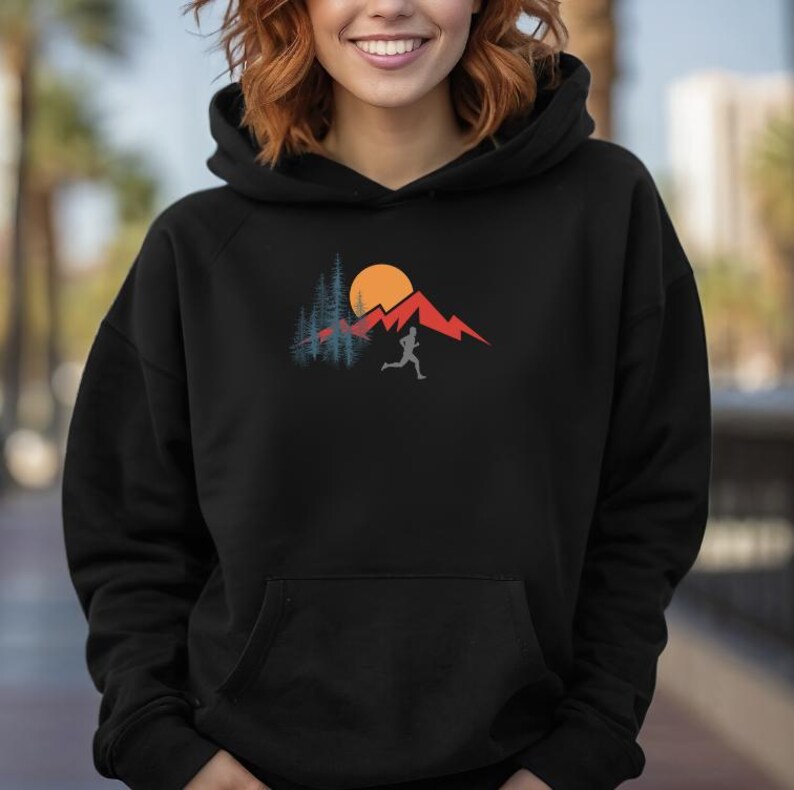 May include: Black hooded sweatshirt with a graphic of a person running in front of a mountain range with a sun and trees.