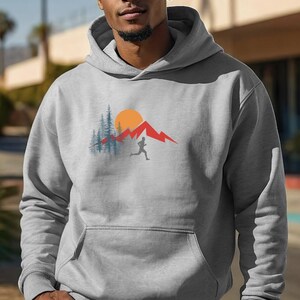 May include: A gray hooded sweatshirt with a graphic design of a person running in front of a mountain range with a sun and trees.