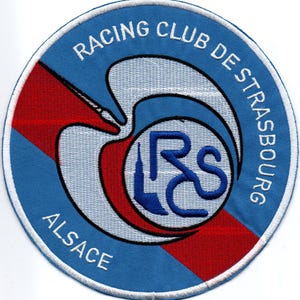 以下が含まれることがあります： 白い円の中に「Racing Club de Strasbourg Alsace」という文字が書かれた青と白の刺繍パッチ。パッチの中央には、青い「RC」の文字が入ったスタイリッシュな鳥が描かれている。