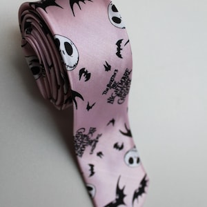 Pode incluir: Gravata rosa claro com um padrão repetido do rosto de Jack Skellington e silhuetas de morcegos. O texto "The Burton's Nightmare Before Christmas" está impresso. A gravata está enrolada.