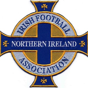 Peut inclure: Écusson brodé représentant le logo de l'Association irlandaise de football. Le design comprend une croix bleue avec les mots "IRISH FOOTBALL" et "NORTHERN IRELAND ASSOCIATION" en lettres blanches, entourée d'une bordure dorée et blanche.
