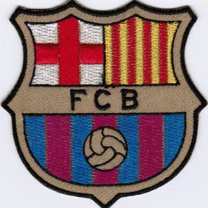 May include: An embroidered patch featuring the FC Barcelona logo. The logo is a shield with a red and yellow striped flag, a white cross, and a soccer ball.