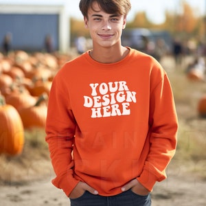 May include: A young person wearing an orange sweatshirt with the text "YOUR DESIGN HERE" in white. The sweatshirt has a crew neck and long sleeves. The person is standing in a field of pumpkins.