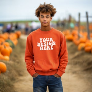 May include: A young person wearing an orange sweatshirt with the text "YOUR DESIGN HERE" in white. The person is standing in a field of pumpkins.