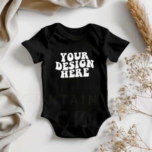 Puede incluir: Un body negro para bebé con mangas cortas y el texto "YOUR DESIGN HERE" en blanco.