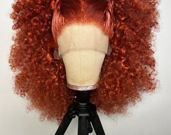 Puede incluir: Una peluca rizada de color naranja brillante con dos coletas en un soporte para pelucas. La peluca está hecha de cabello sintético y tiene un frente de encaje.