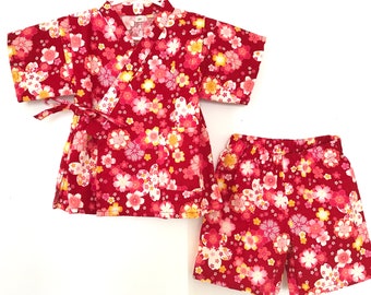 May include: Red and white floral print two-piece outfit for a baby or toddler. The top is a kimono style with short sleeves and a tie closure. The bottom is a pair of shorts.