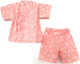 May include: A pink and white floral print two-piece outfit for a child. The top is a kimono style with short sleeves and a tie at the waist. The shorts have an elastic waistband.