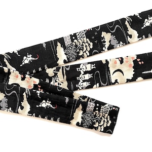 May include: Black fabric with a white and pink pattern of trees, buildings, and people. The fabric is folded in thirds.