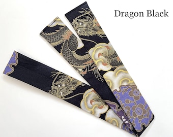 May include: Two long, rectangular fabric strips featuring a black background with a detailed dragon motif, gold accents, and purple floral patterns. The text Dragon Black is printed in the upper right corner of the image.