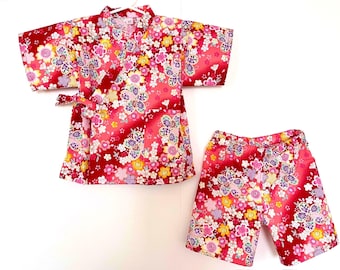 May include: A two-piece outfit consisting of a short-sleeved wrap-style top and matching shorts. The fabric is a vibrant red featuring a dense, multicolored floral pattern with pink, yellow, and white blossoms. The top includes a side tie closure.