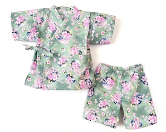 May include: A green and pink floral print two-piece pajama set for children. The top is a kimono style with a tie closure. The bottom is a pair of shorts.