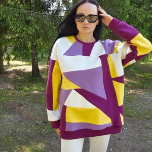 May include: A purple, yellow, and white geometric patterned sweatshirt with long sleeves and a crew neck.