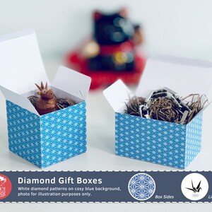 以下が含まれることがあります： 白い蓋と青いダイヤモンド模様の、開いた正方形のギフトボックスが2つ。1つの箱には小さな茶色の置物、もう1つには金属製のオブジェクトが入っています。画像には「Diamond Gift Boxes」と書かれています。