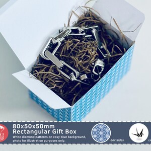 以下が含まれることがあります： 青い背景に白いダイヤモンド模様の長方形ギフトボックス。銀色のチェーンと茶色の紙の詰め物が入っています。ボックスのサイズは80x50x50mmです。