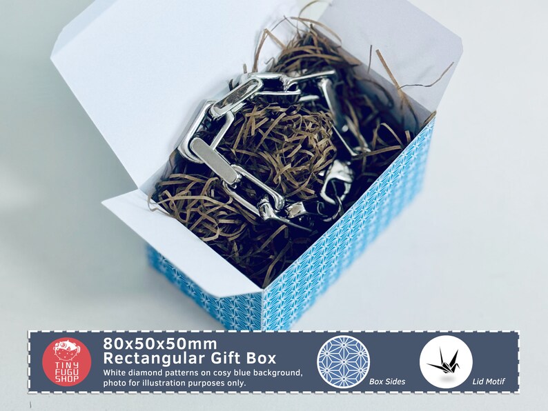 以下が含まれることがあります： 青い背景に白いダイヤモンド模様の長方形ギフトボックス。銀色のチェーンと茶色の紙の詰め物が入っています。ボックスのサイズは80x50x50mmです。