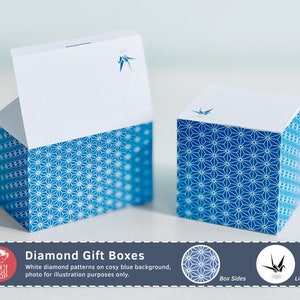 以下が含まれることがあります： 立方体のギフトボックスが2つ。ボックスは白い上部と、白いダイヤモンド模様の青いベースがあります。各ボックスの上部には青い鶴のデザインがあります。画像には「Diamond Gift Boxes」と書かれています。