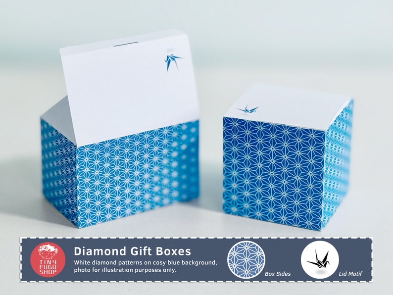 以下が含まれることがあります： 立方体のギフトボックスが2つ。ボックスは白い上部と、白いダイヤモンド模様の青いベースがあります。各ボックスの上部には青い鶴のデザインがあります。画像には「Diamond Gift Boxes」と書かれています。