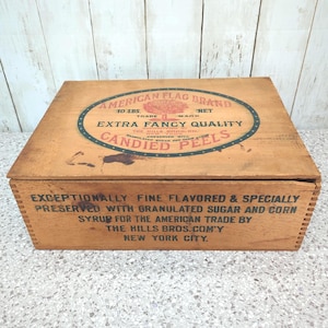 May include: A rectangular wooden crate with a lid featuring a printed oval label that reads American Flag Brand 10 Lbs. Net Extra Fancy Quality Candied Peels. The front side text reads Exceptionally Fine Flavored & Specially Preserved With Granulated Sugar And Corn Syrup For The American Trade By The Hills Bros. Com'y New York City.