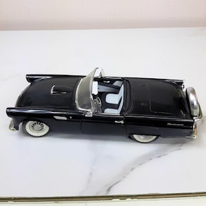 Puede incluir: Modelo de coche Ford Thunderbird convertible negro de 1957. El coche tiene un interior blanco y la palabra "Thunderbird" es visible en la parte trasera.