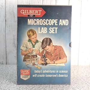 Könnte beinhalten: Ein Vintage-Karton für ein Gilbert Microscope and Lab Set mit einer Illustration von zwei Kindern bei Experimenten. Die blaue Schachtel zeigt den Text Microscope and Lab Set, Gilbert und den Slogan today's adventures in science will create tomorrow's America.